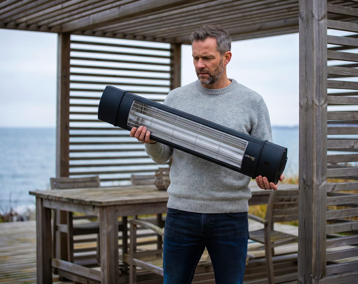 Man håller Opranic PRO V70 infravärmare under pergola och planerar väggmontage