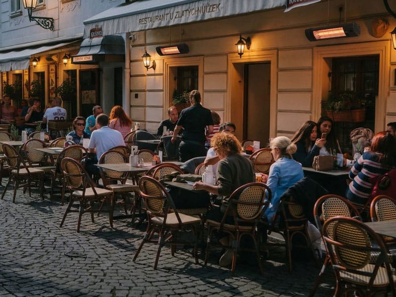 Opranic Infrarot-Heizstrahler an einer Restaurantfassade über der Außengastronomie im Abendlicht, Gäste sitzen dank gleichmäßiger Strahlungswärme komfortabel im Freien